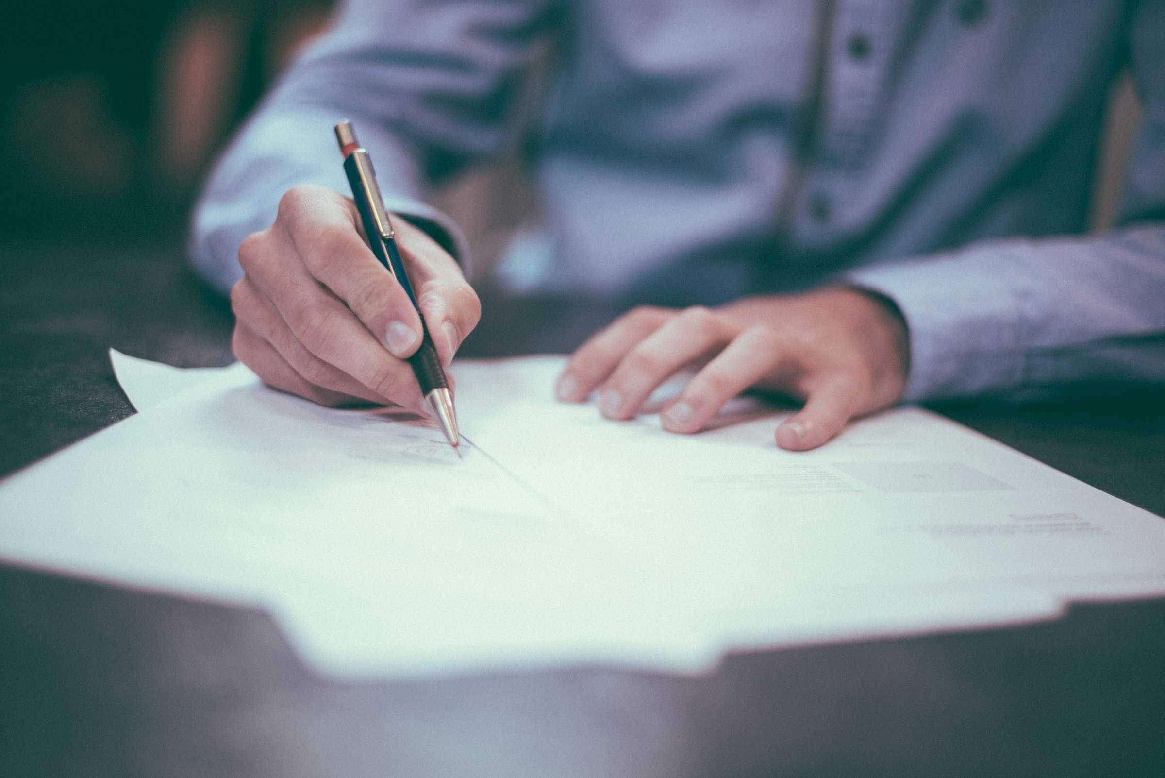 Persona firmando documentos sobre un escritorio